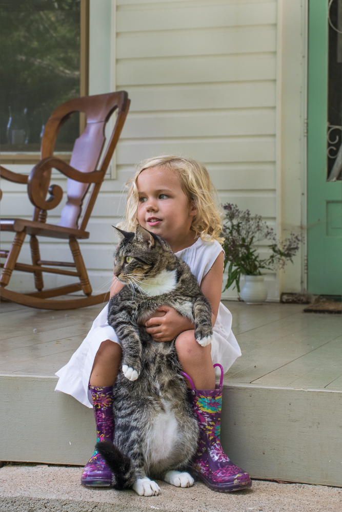 Portrait of a little girl playing with her cat on the front porch.