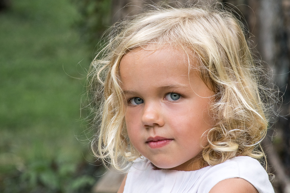 A close-up portrait of a little girl playing outside in the summer heat.