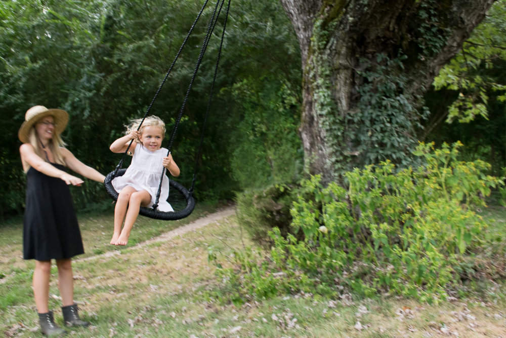 A mother pushes her daughter in a swing at their farm house.