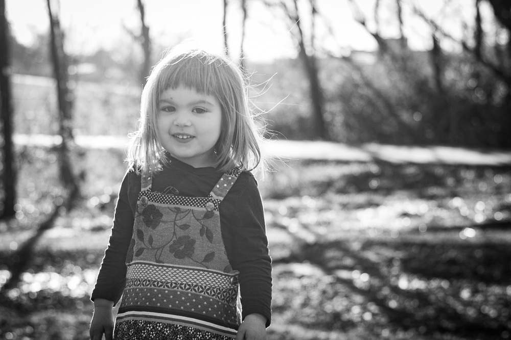Young girl playing in the sunlight near the woods.