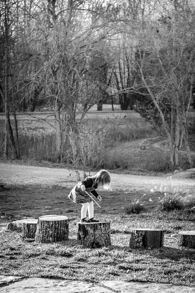 A young girl jumps from stump to stump at a natural playground.