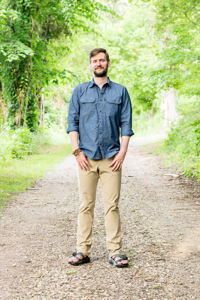 A man stands on a dirt path in the woods.