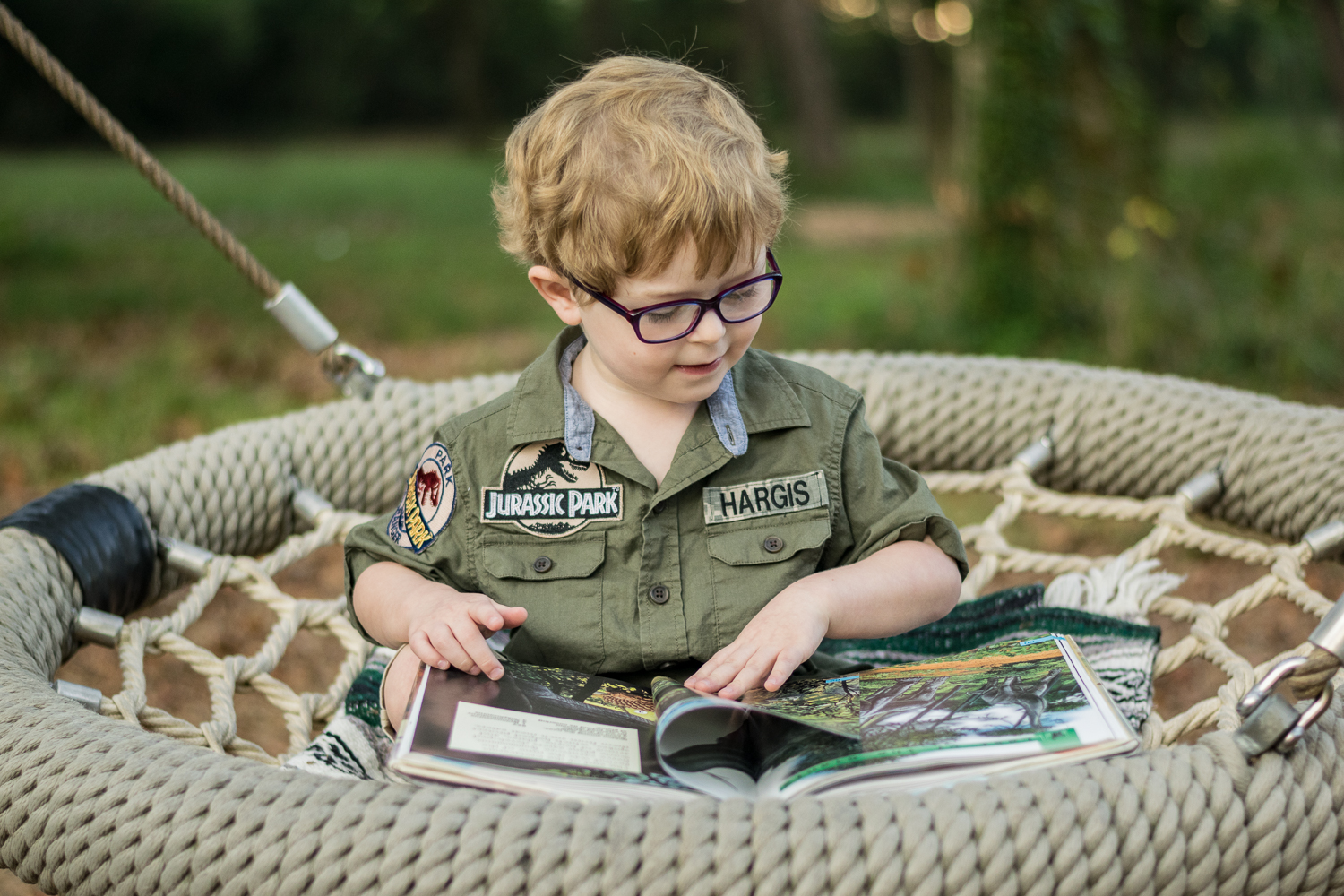 Young boy reading a dinosaur book in a large mesh swing.