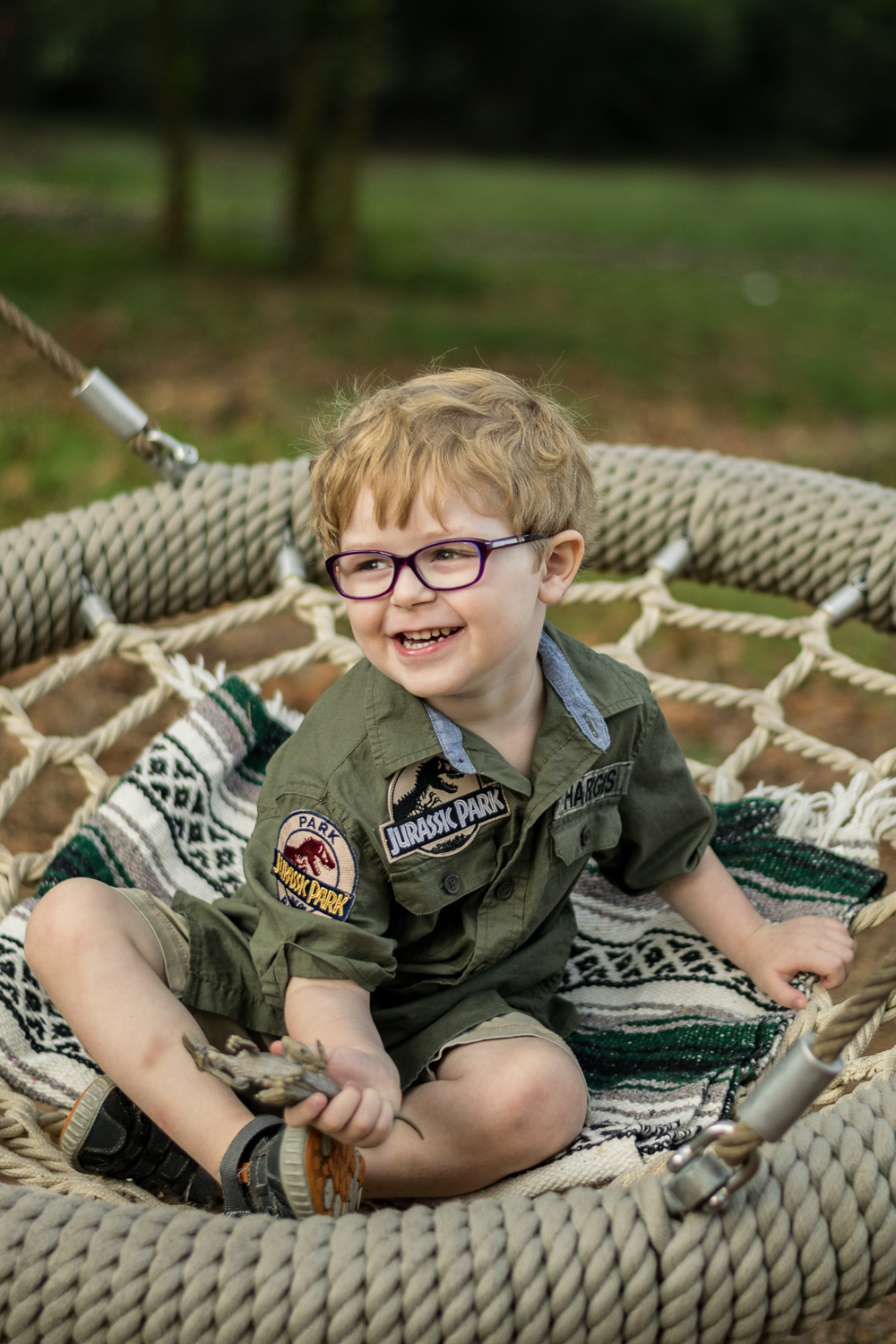 A young boy plays with his dinosaur in a swing at Baker Creek Preserve.