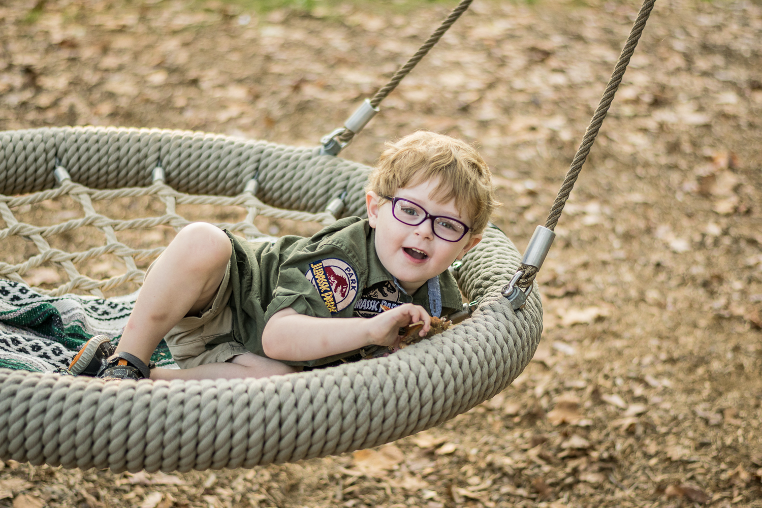 A young boy playing with his dinosaur in a large rope swing.