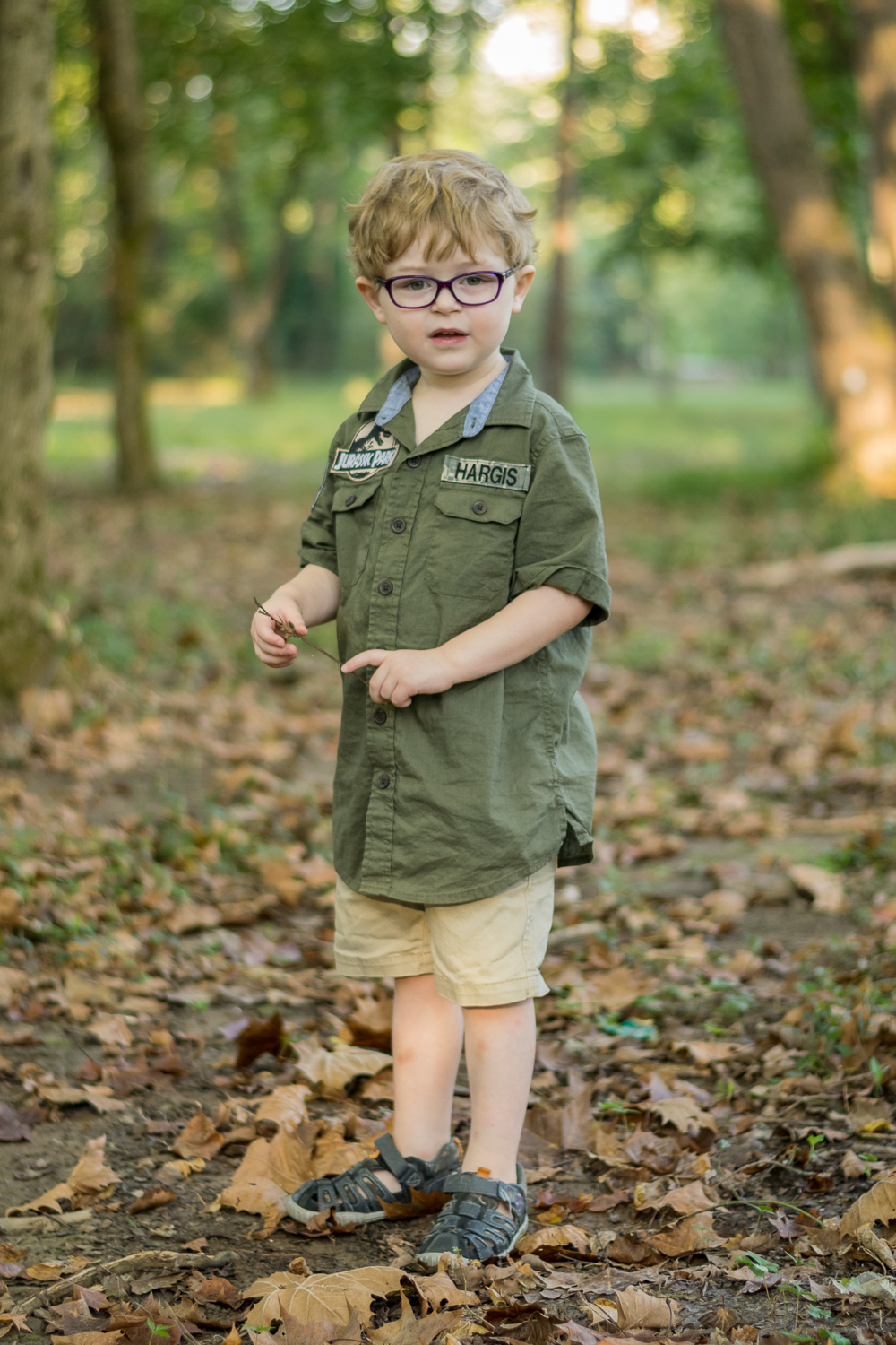 A young boy stands in the forest and holds a stick.