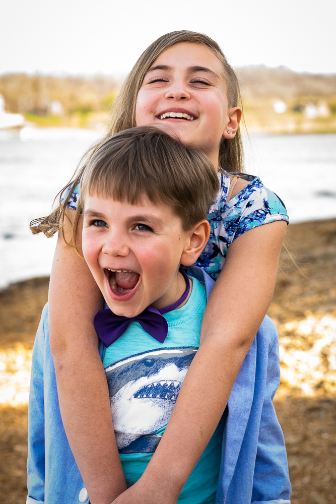 Siblings laughing along a river shoreline.