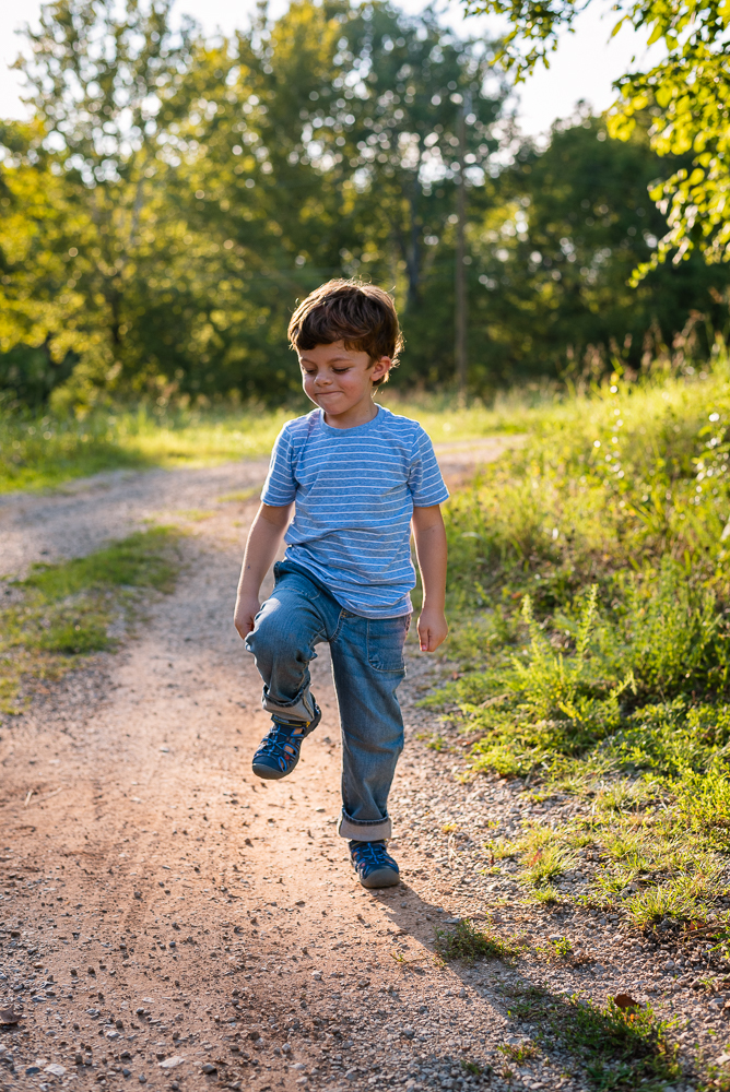 A little boy stomps along a gravel road in the sunshine.