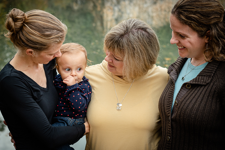 Three generations of women and a baby stand together in front of a lake.