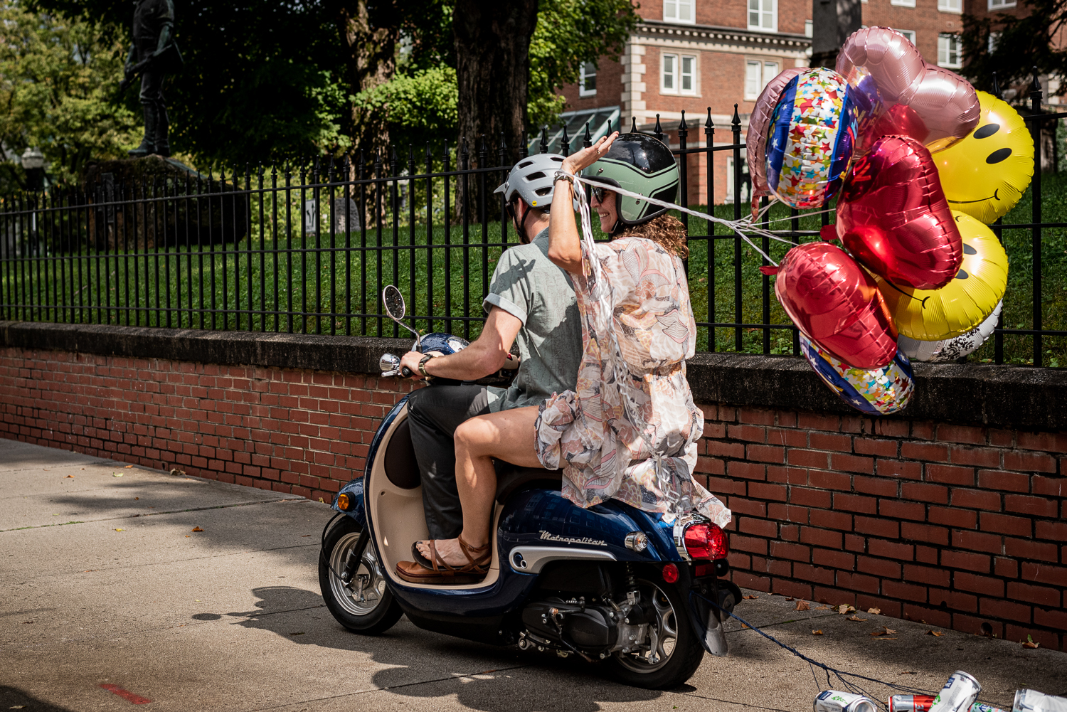 A newly married couple ride away on a scooter with balloons.
