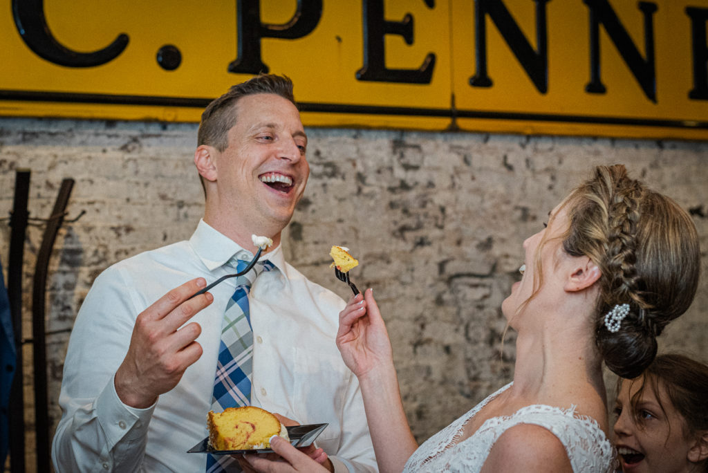 A bride and groom laugh as they feed each other cake at Maple Hall Bowling Alley.