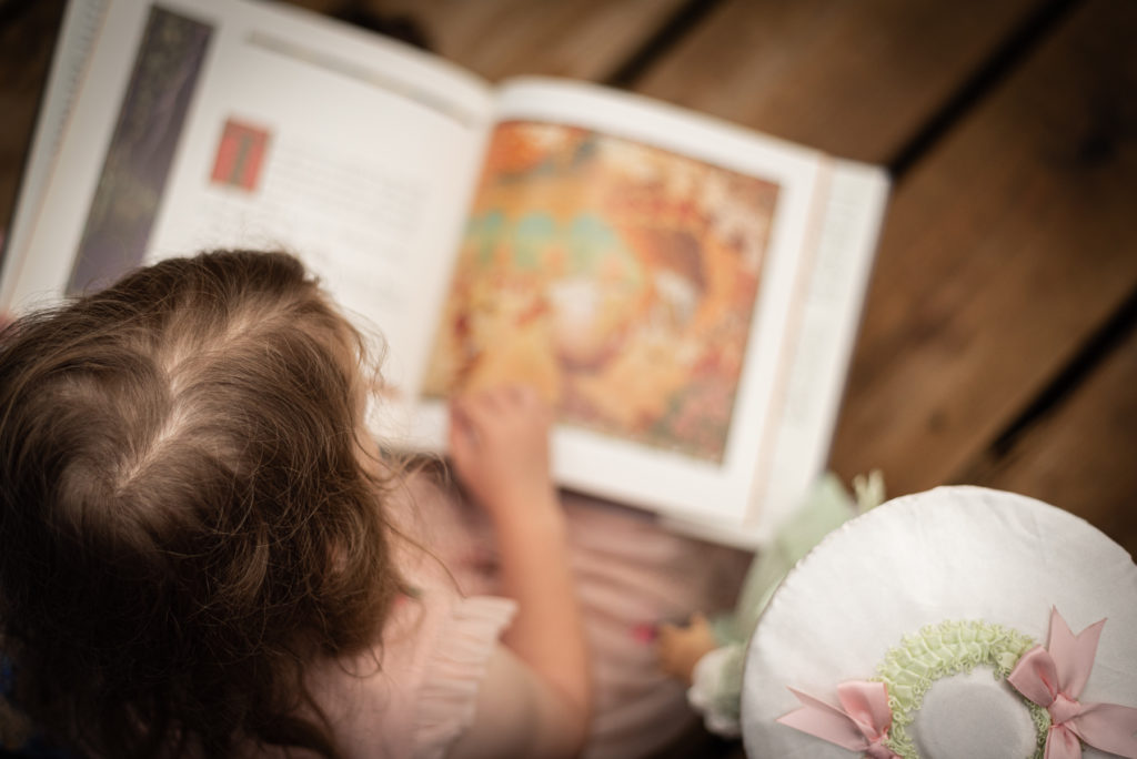 A little girl reads a book with her doll.