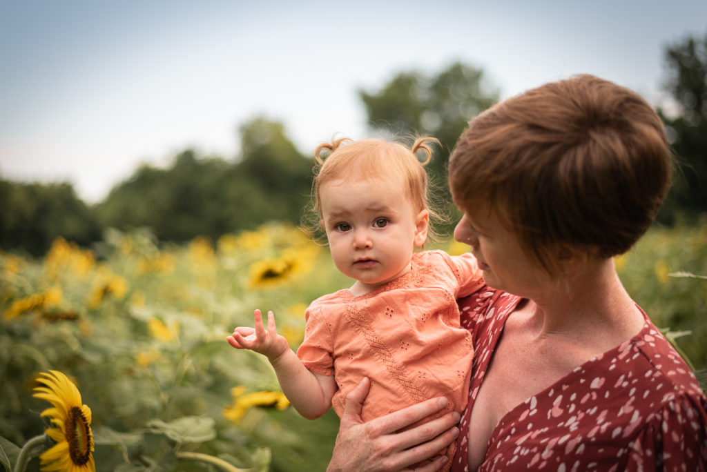 A young mother holds her toddler in a sunflower field.