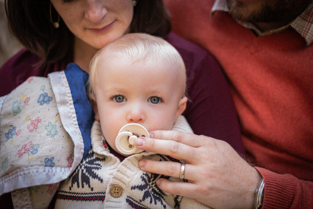 A toddler with his pacifier being held by his parents.