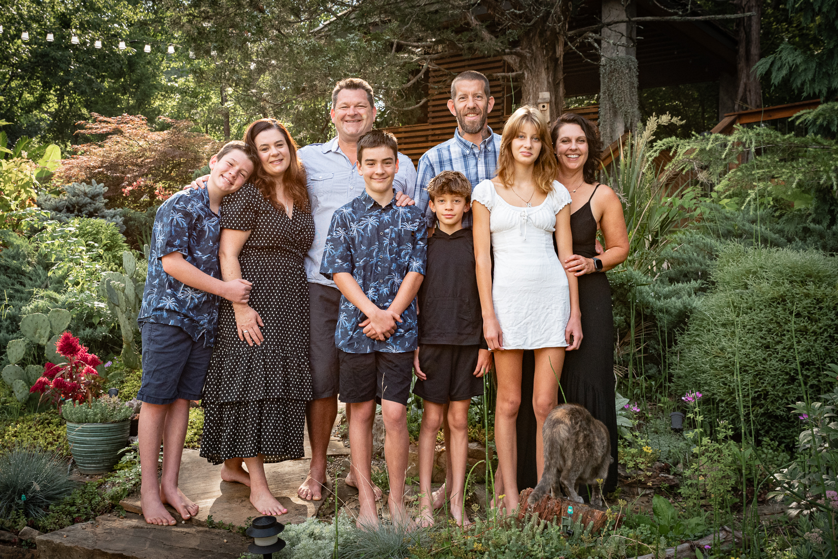 A brother, sister, and their families stand together in the lush, green back yard.