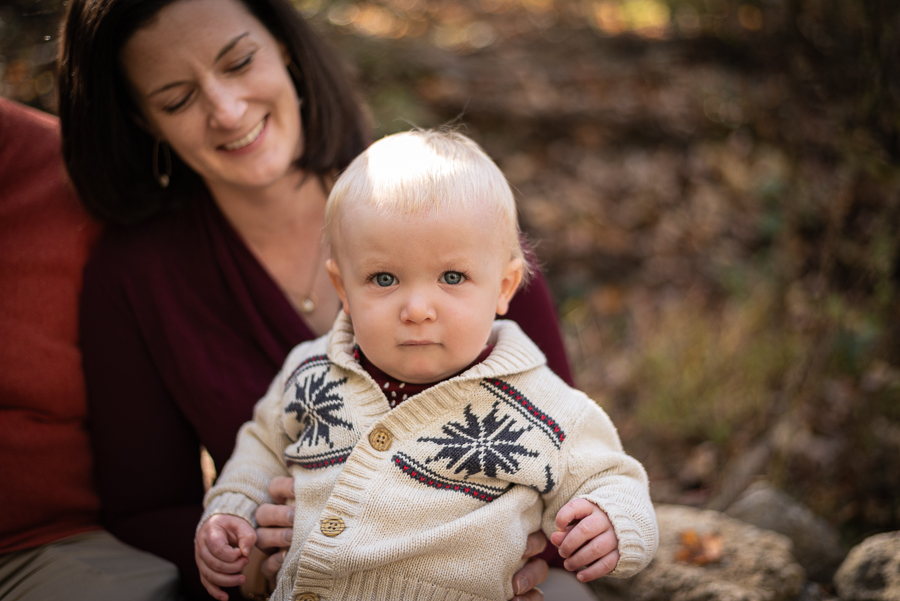 A mother holds her baby son on her lap in the forest.