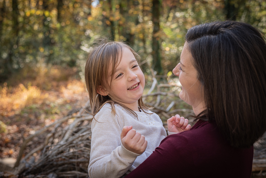 A mother holds her smiling daughter in the forest.