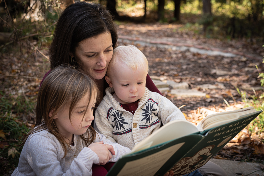 A mother and her two small children read a book in the forest.