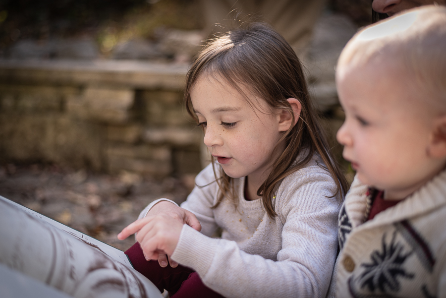 A little girl reads to her mother and baby brother.